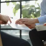 Manos revisando un documento, discutiendo cómo pedir nota simple.