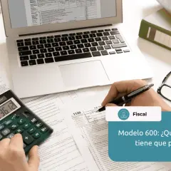 Calculadora, gafas, portátil y documentos fiscales sobre un escritorio.