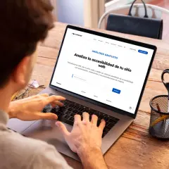 Persona usando laptop para obtener un informe de accesibilidad web. La pantalla muestra "Analiza la accesibilidad de tu sitio web".