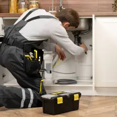 Fontanero revisa tuberías bajo el fregadero, recordándonos las **cosas que cubre el seguro de hogar y no sabemos**.