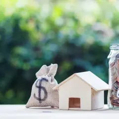 Saco de dinero, casa de madera y frasco lleno de monedas, simbolizando el pleno dominio de tus finanzas para adquirir tu hogar.