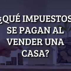 ¿Qué impuestos se pagan al vender una casa? Mano colocando monedas en una alcancía con una casa de madera y una planta.