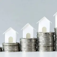 Casas blancas en pilas de monedas crecientes. Esto ilustra el concepto de LTV (Loan-to-Value) y cómo el valor de una propiedad puede aumentar con el tiempo.