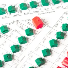 Casas de juguete verdes y rojas sobre planos de parcelas, simulando la compra de viviendas y el tipo de interés de las hipotecas.