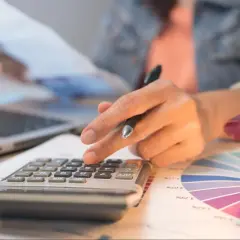 Persona calcula con calculadora y portátil, revisando gráficos. Quizás planeando una hipoteca puente Santander.