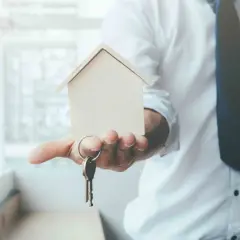 Un hombre con camisa blanca y corbata oscura ofrece una maqueta de casa y llaves, simbolizando el usufructo de una vivienda.