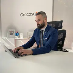 Hombre de negocios trabajando en su portátil en una oficina con el logo de Grocasa. Busca opiniones sobre Grocasa para su próximo proyecto.