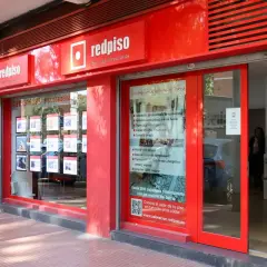 Redpiso, inmobiliaria con opiniones positivas. Fachada roja, escaparate con anuncios de pisos y dos mujeres mirando.