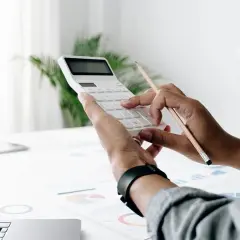 Persona calcula el valor tasación vivienda a efectos del seguro con calculadora y lápiz sobre gráficos.