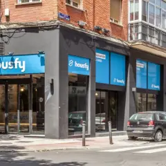Fachada de oficina de Housfy, con letreros azules y blancos. Las opiniones sobre Housfy son positivas, como se ve en su presencia en la calle.