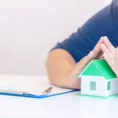 Manos protegiendo una maqueta de casa, con un portapapeles y bolígrafo en primer plano. Un ejemplo de derecho de retracto.