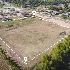 Un terreno es un bien inmueble. Vista aérea de un gran terreno vacío delimitado por puntos y líneas discontinuas, con casas y vegetación alrededor.