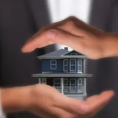Manos protegen una maqueta de casa, simbolizando lo que se necesita para tasar una vivienda: cuidado y análisis.