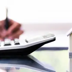 Un tasador homologado calcula el valor de una casa modelo con una calculadora.