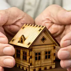 Manos protegen una maqueta de casa, simbolizando el usufructo del 50% de una vivienda.