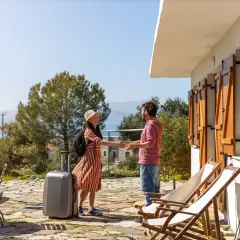 Pareja sonriendo y dándose la mano, con maleta lista para una permuta de viviendas entre particulares. Vacaciones soleadas.