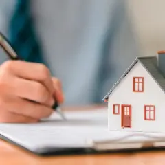 Maqueta de casa sobre documento con mano firmando.