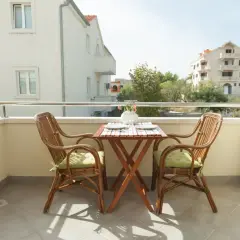 Balcón con mesa y sillas de mimbre, vistas a edificios con ventanas y balcones, elementos comunes de un edificio.