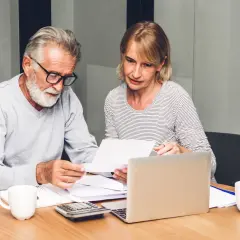 Pareja mayor revisa documentos, buscando tranquilidad con un seguro de protección de pagos.