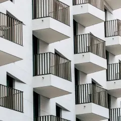 Fachada moderna de edificio con balcones escalonados. Cada balcón tiene una barandilla de metal y una mesa con sillas, ideal para una cuenta vivienda.