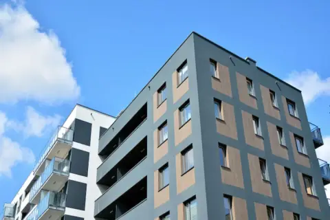 Edificios modernos con balcones de cristal y una fachada con división horizontal de paneles de madera y ventanas.