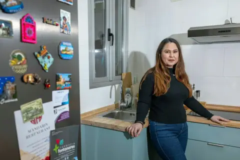 Mujer en cocina, con imanes de viajes en la nevera. Una opción para tu futuro hogar: alquiler con opción a compra entre particulares.