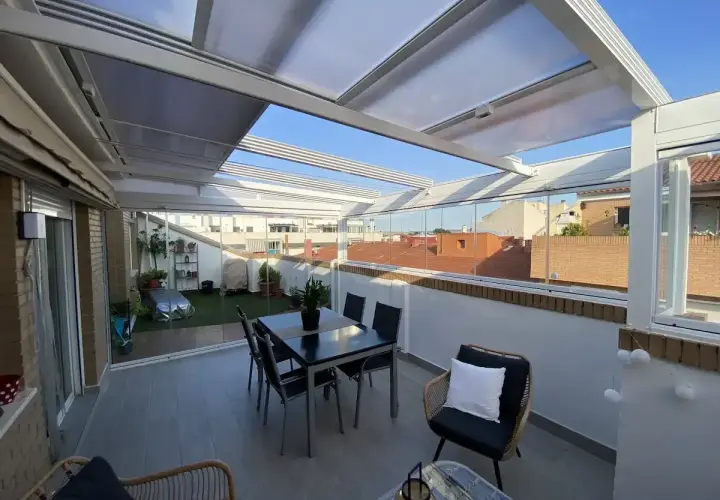 Cerramiento terraza casa unifamiliar con mesa y sillas, y zona ajardinada. Disfruta del exterior todo el año.