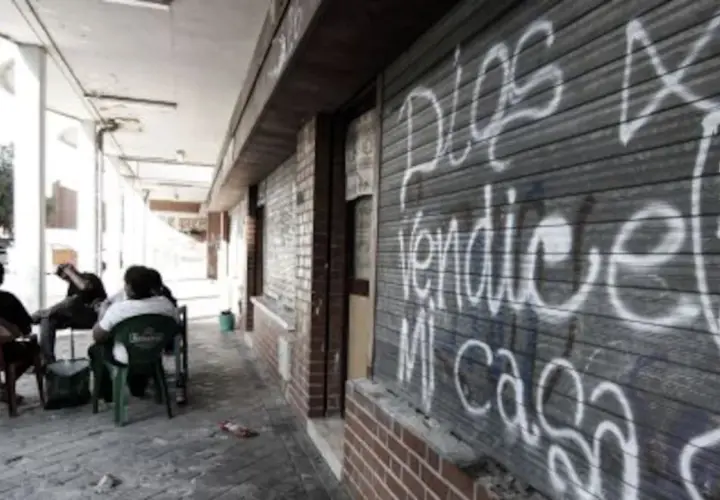 Gente sentada en sillas de plástico frente a un local con grafitis, reflejo de los peores barrios de Madrid.