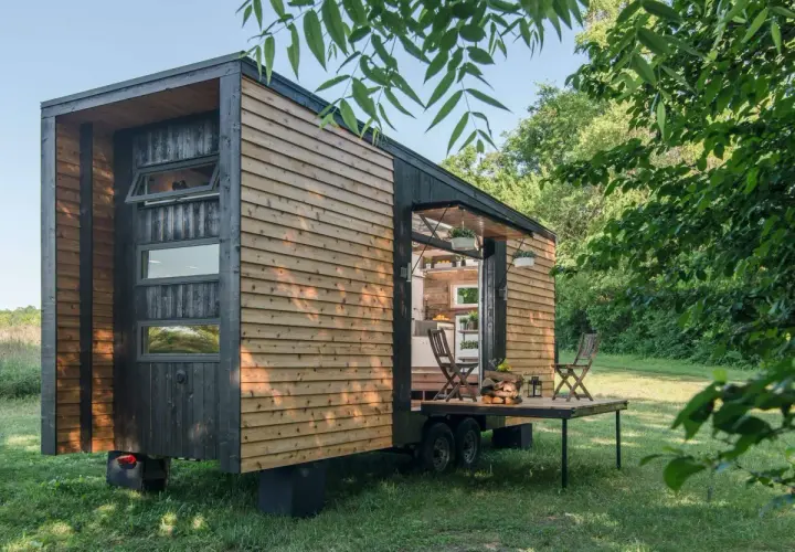 Casa móvil moderna de madera, ideal para quienes buscan qué se puede construir en terreno rústico. Tiene una terraza desplegable y está rodeada de vegetación.