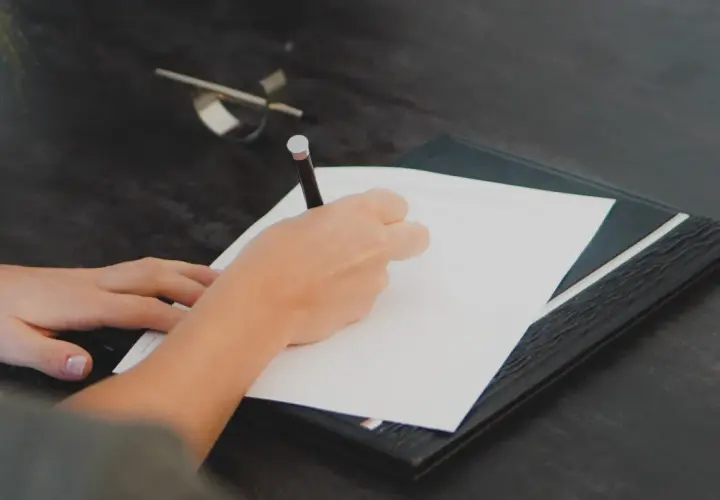 Mano escribiendo en un documento. Cualquier persona interesada en saber quién puede pedir una nota simple, puede hacerlo para verificar información.