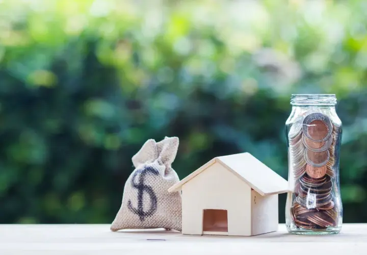 Saco de dinero, casa de madera y frasco lleno de monedas, simbolizando el pleno dominio de tus finanzas para adquirir tu hogar.