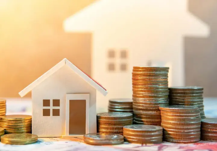 Casas pequeñas y pilas de monedas, sugiriendo ahorro para la transferencia OMF compraventa de una vivienda.