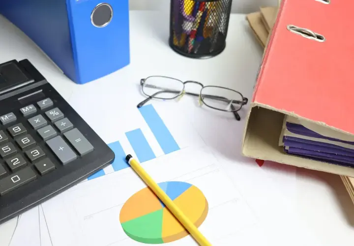 Calculadora, gráficos y carpetas sobre un escritorio. Analizando el tipo de interés actual para tomar decisiones financieras.