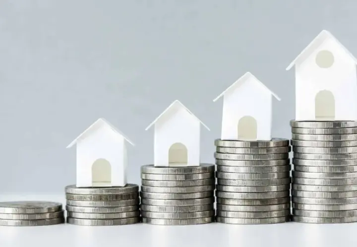 Casas blancas en pilas de monedas crecientes. Esto ilustra el concepto de LTV (Loan-to-Value) y cómo el valor de una propiedad puede aumentar con el tiempo.