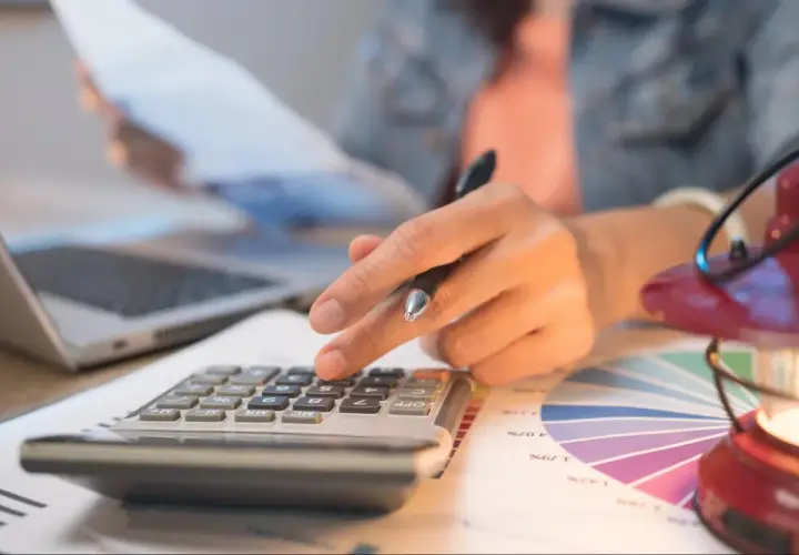 Persona calcula con calculadora y portátil, revisando gráficos. Quizás planeando una hipoteca puente Santander.