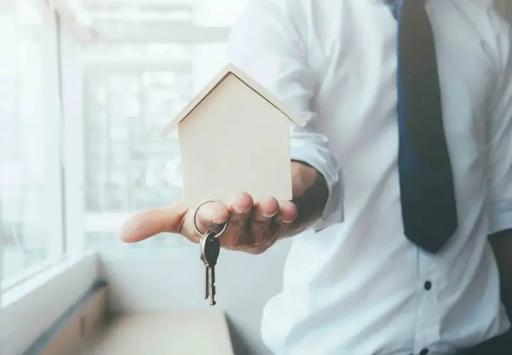 Un hombre con camisa blanca y corbata oscura ofrece una maqueta de casa y llaves, simbolizando el usufructo de una vivienda.