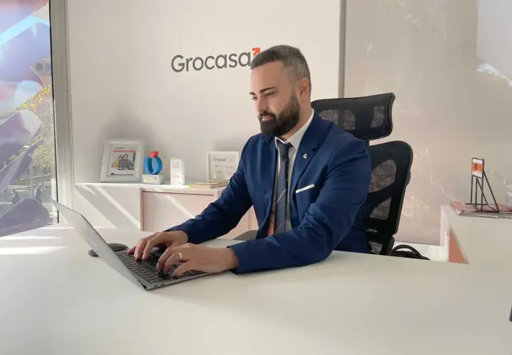 Hombre de negocios trabajando en su portátil en una oficina con el logo de Grocasa. Busca opiniones sobre Grocasa para su próximo proyecto.