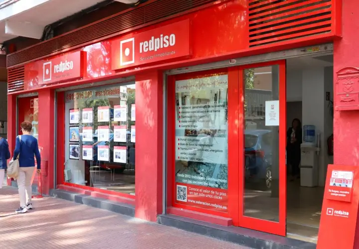 Redpiso, inmobiliaria con opiniones positivas. Fachada roja, escaparate con anuncios de pisos y dos mujeres mirando.