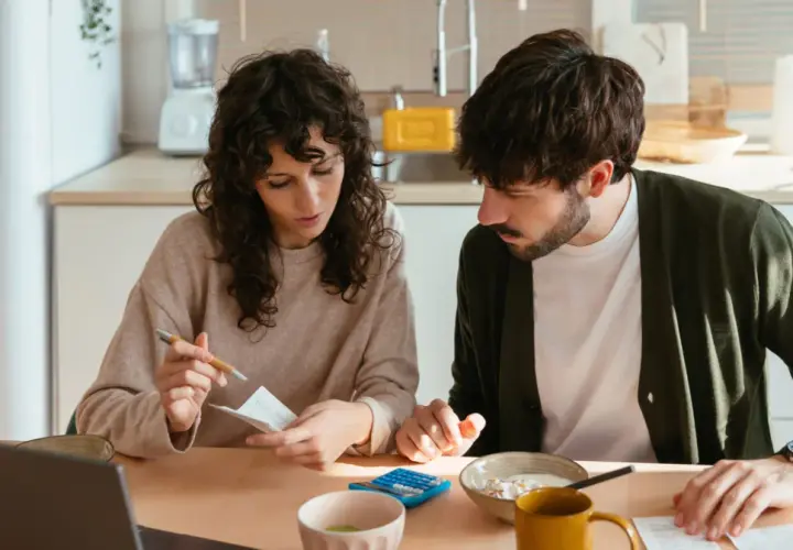 Pareja revisando facturas y usando calculadora, gestionando su comunidad de bienes entre familiares.
