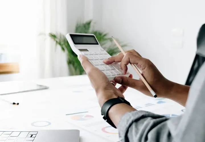 Persona calcula el valor tasación vivienda a efectos del seguro con calculadora y lápiz sobre gráficos.