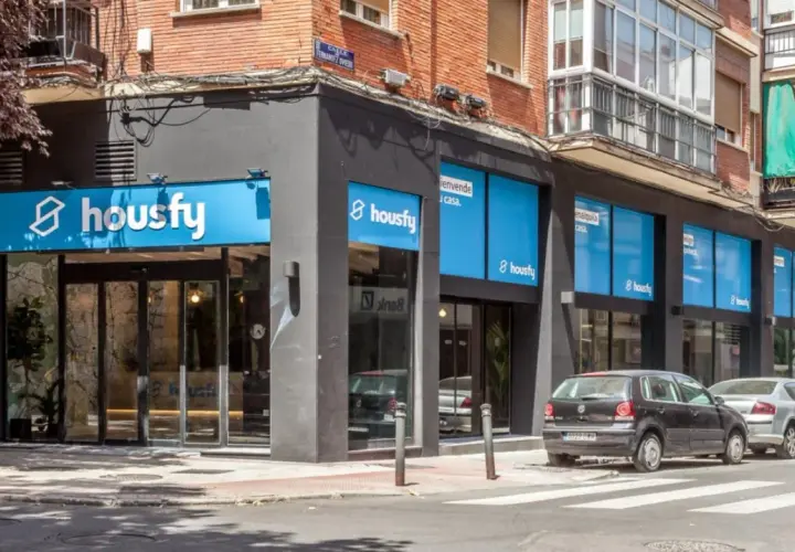 Fachada de oficina de Housfy, con letreros azules y blancos. Las opiniones sobre Housfy son positivas, como se ve en su presencia en la calle.