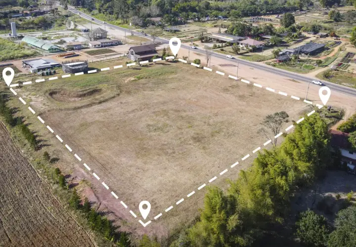Un terreno es un bien inmueble. Vista aérea de un gran terreno vacío delimitado por puntos y líneas discontinuas, con casas y vegetación alrededor.