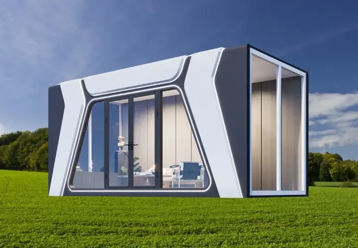 Moderna casa cápsula con grandes ventanales, ubicada en un campo verde bajo un cielo azul.