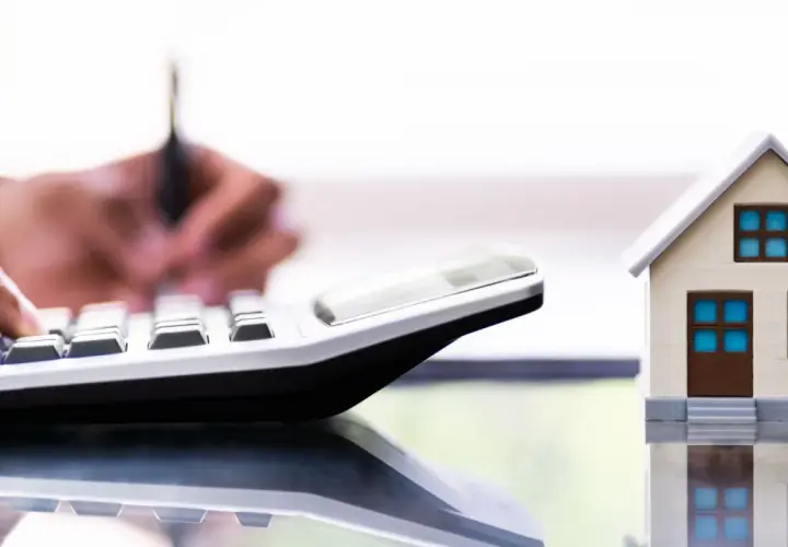 Un tasador homologado calcula el valor de una casa modelo con una calculadora.