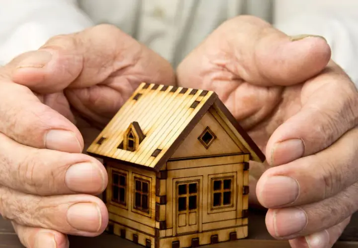 Manos protegen una maqueta de casa, simbolizando el usufructo del 50% de una vivienda.