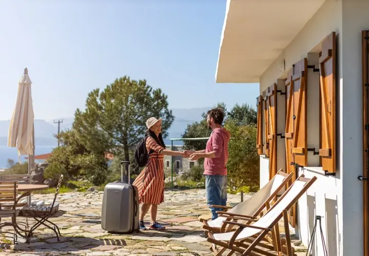 Pareja sonriendo y dándose la mano, con maleta lista para una permuta de viviendas entre particulares. Vacaciones soleadas.
