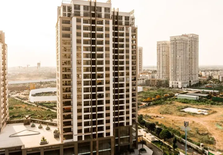 Edificios modernos se alzan sobre un **terreno urbano no consolidado**, con vegetación y construcciones en proceso.