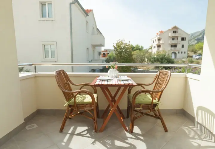 Balcón con mesa y sillas de mimbre, vistas a edificios con ventanas y balcones, elementos comunes de un edificio.