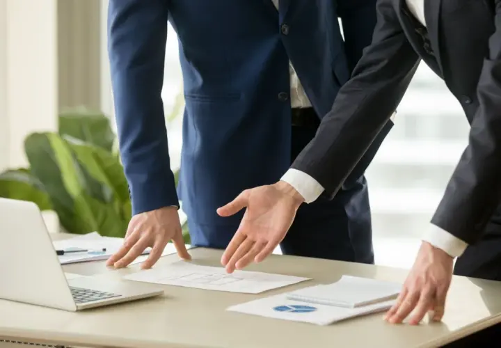 Dos hombres de negocios analizan un plano. Se discute el precio del informe pericial arquitecto.