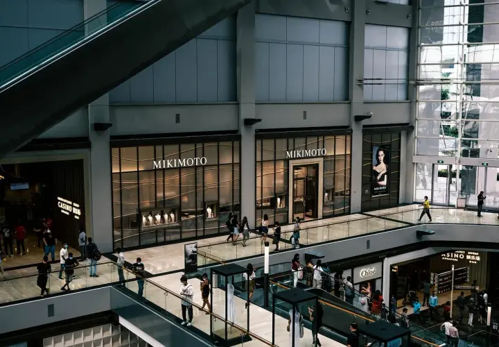 Interior de centro comercial con escaleras mecánicas y tiendas de lujo. La tasación de locales comerciales es clave para el valor de estos espacios.